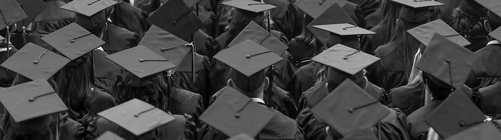 Image of graduates highlighting caps, tassles, and gowns. Image is taken from behind.