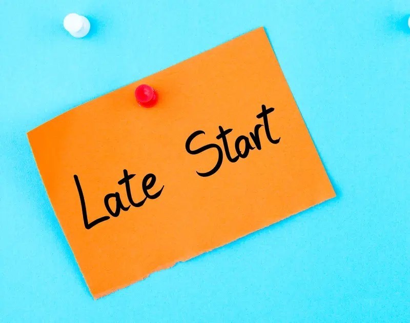 Image of note on orange piece of paper that says late start on blue background. there are two push pins holding the note in place. One is white and the other is red.