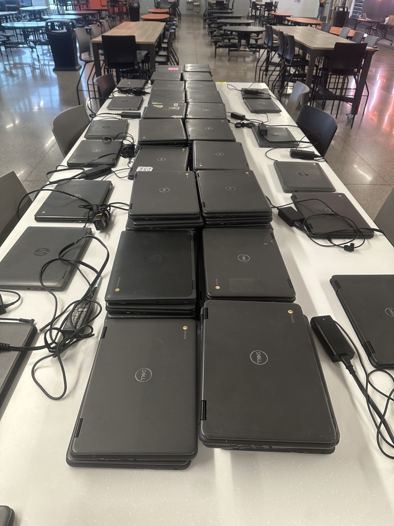 Picture of stacks of chromebooks and chargers on a table.