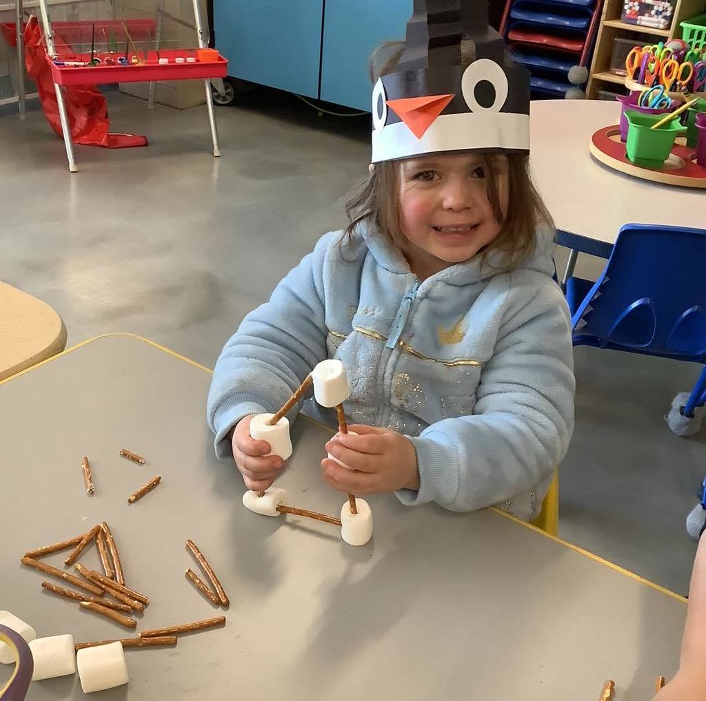 picture of girl building with stick pretzels and marshmallows while wearing her penguin hat