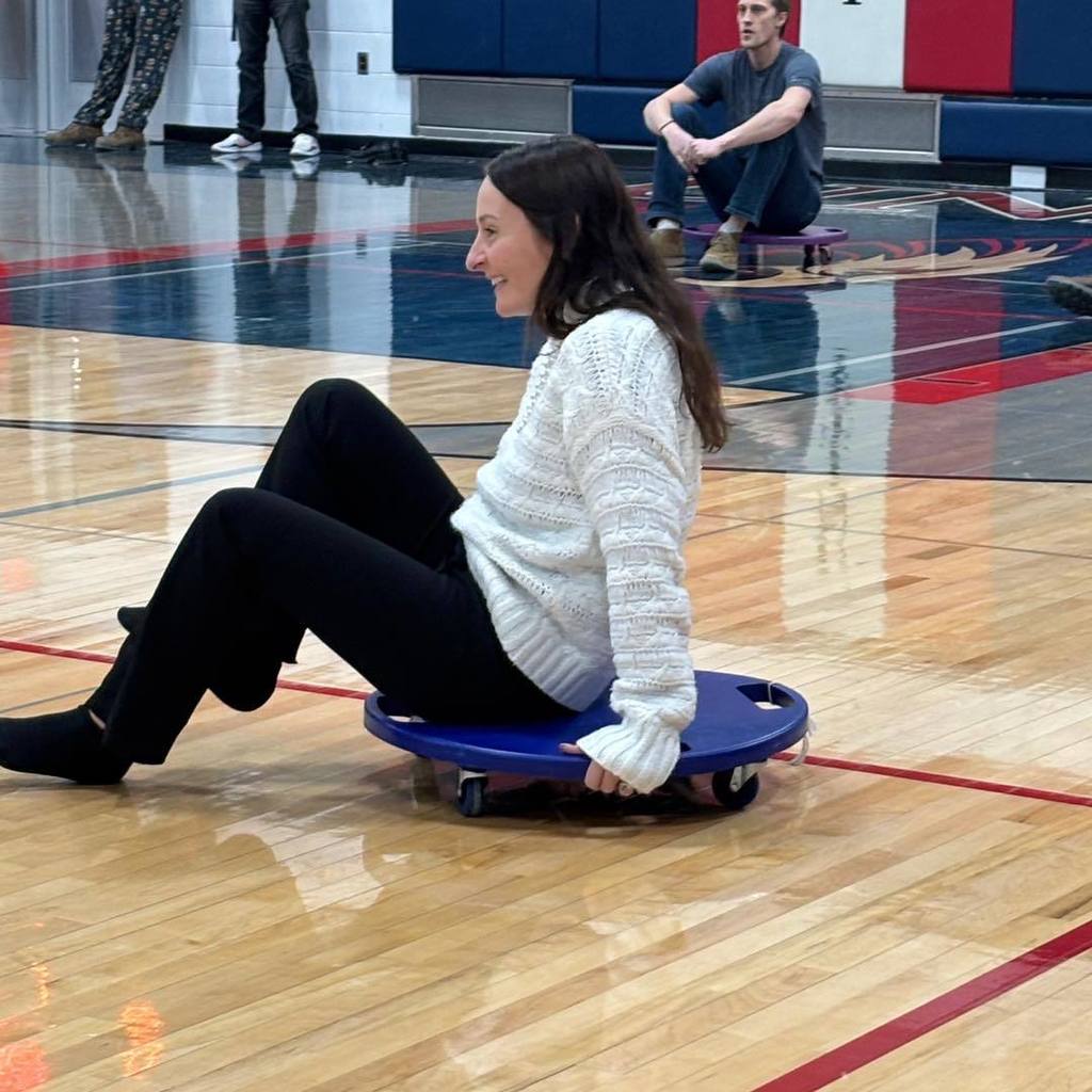 picture of Mrs. Mackey riding a scooter in the gym