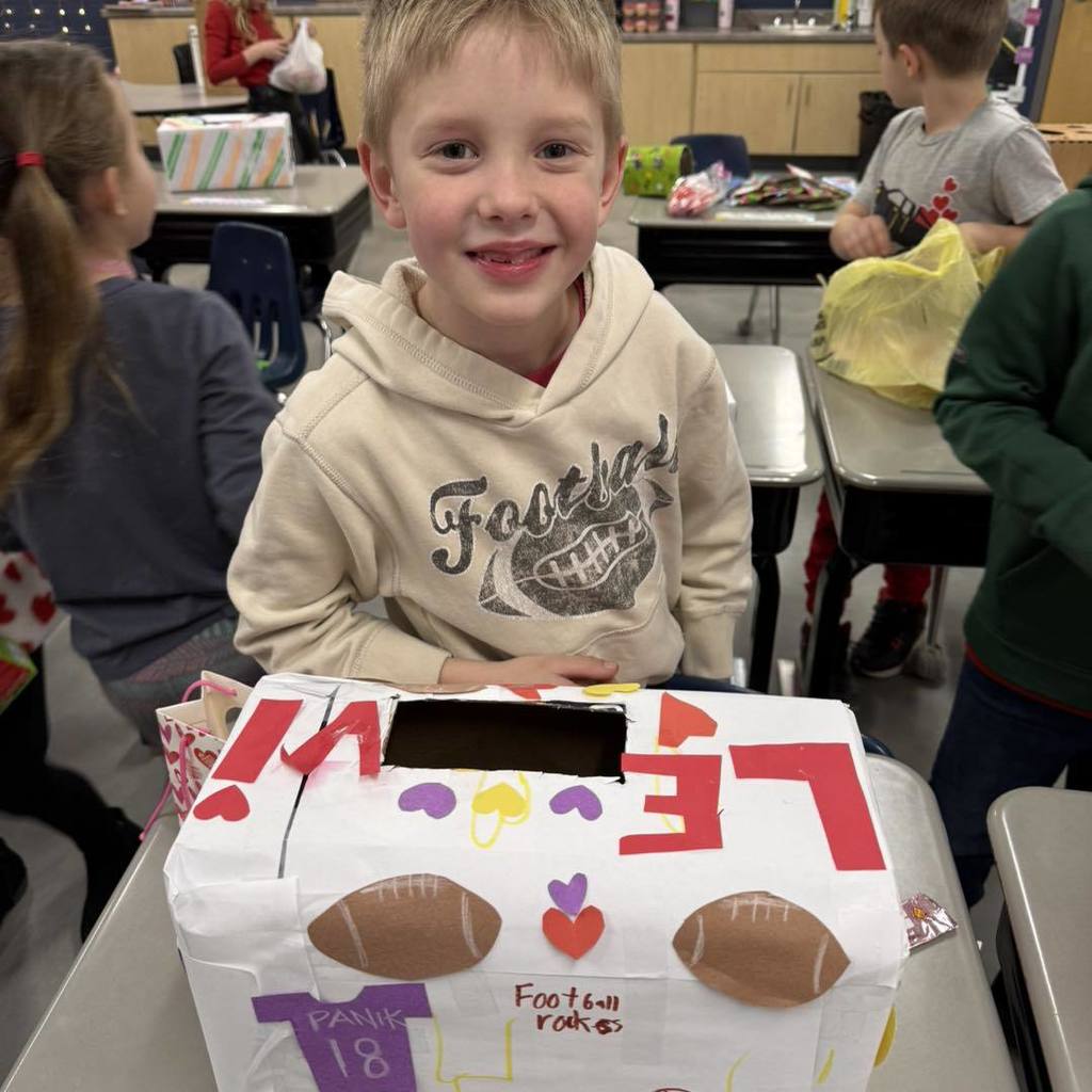 picture of A student smiling with his football-themed Valentine's Day box decorated with stickers and a jersey number.