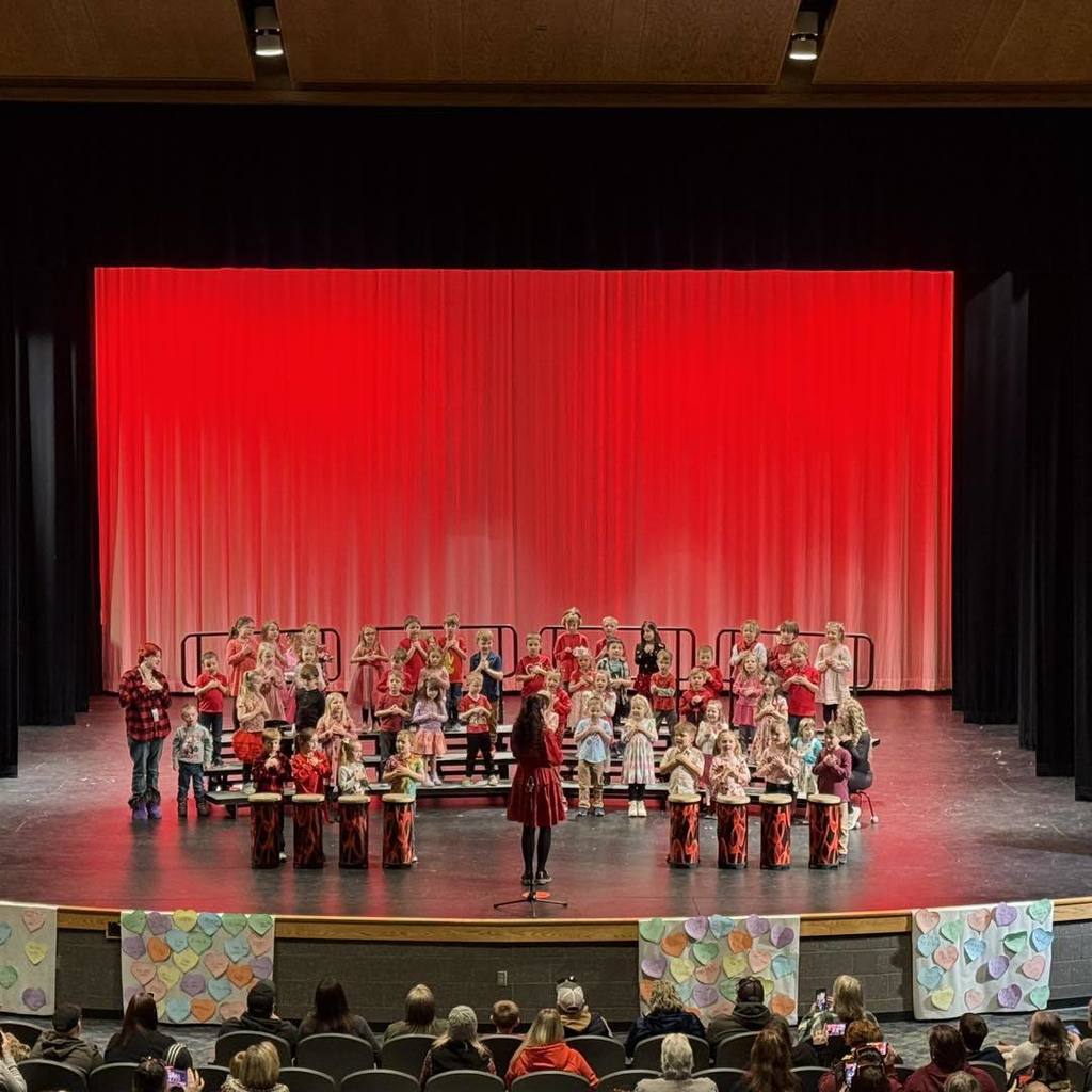 Kindergarten students performing on stage with red curtains for their Valentine's Day Concert