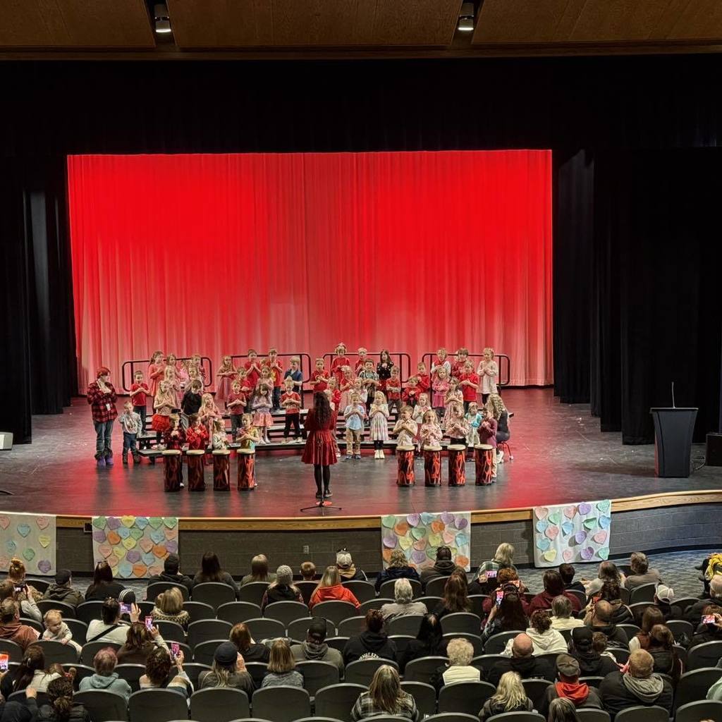 Kindergarten students performing on stage with red curtains for their Valentine's Day Concert