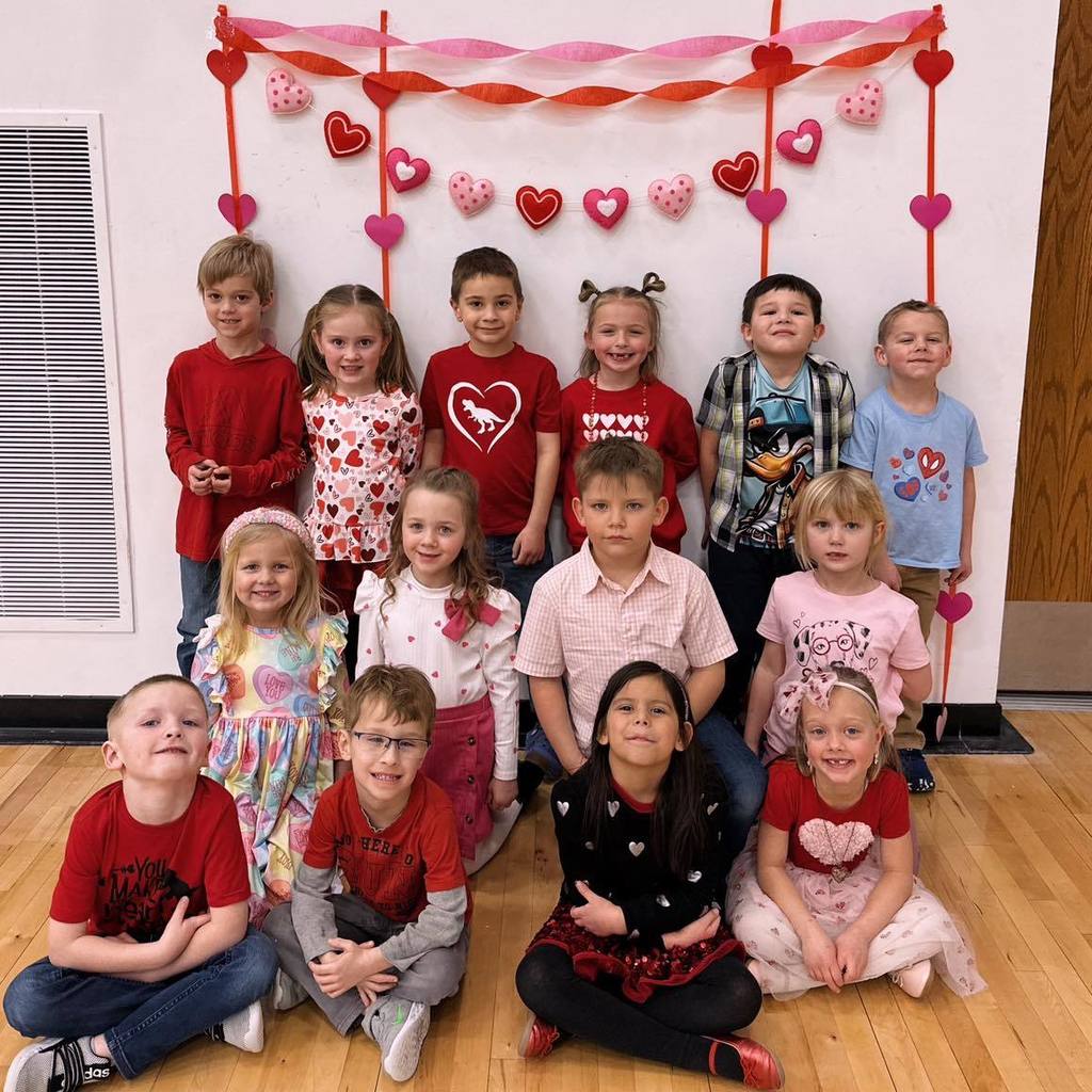A group of Unity kindergarten students in festive red and pink outfits posing together in front of heart decorations