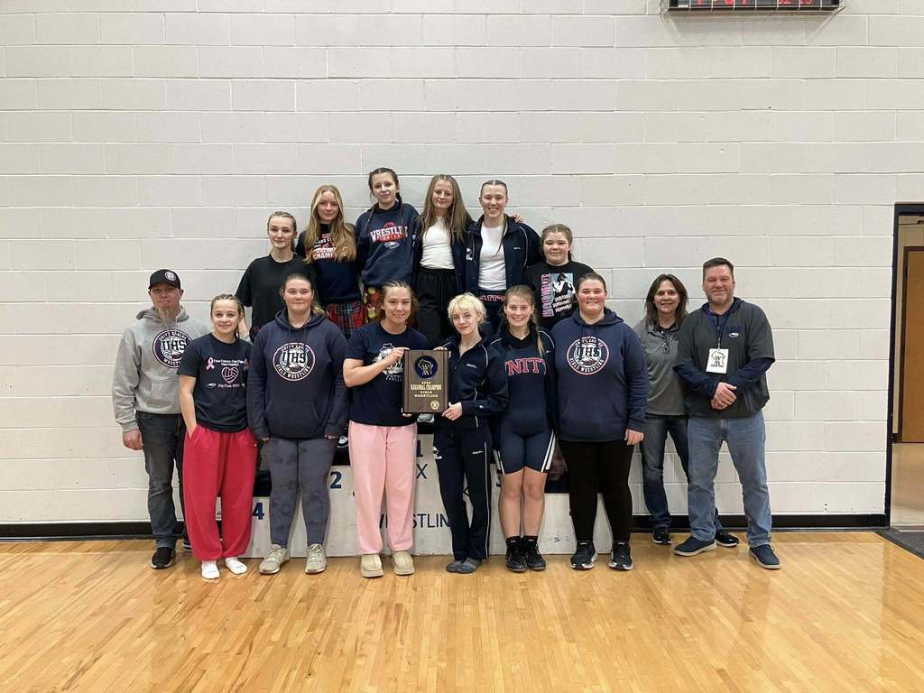 The Unity Eagles girls wrestling team and coaches posing together for a group photo on the gym floor after winning the Regional Championship