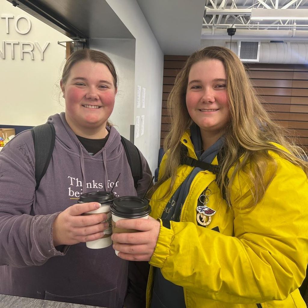 Two smiling Unity students holding their coffee cups from the Raise Your Voice! Club pop-up bar