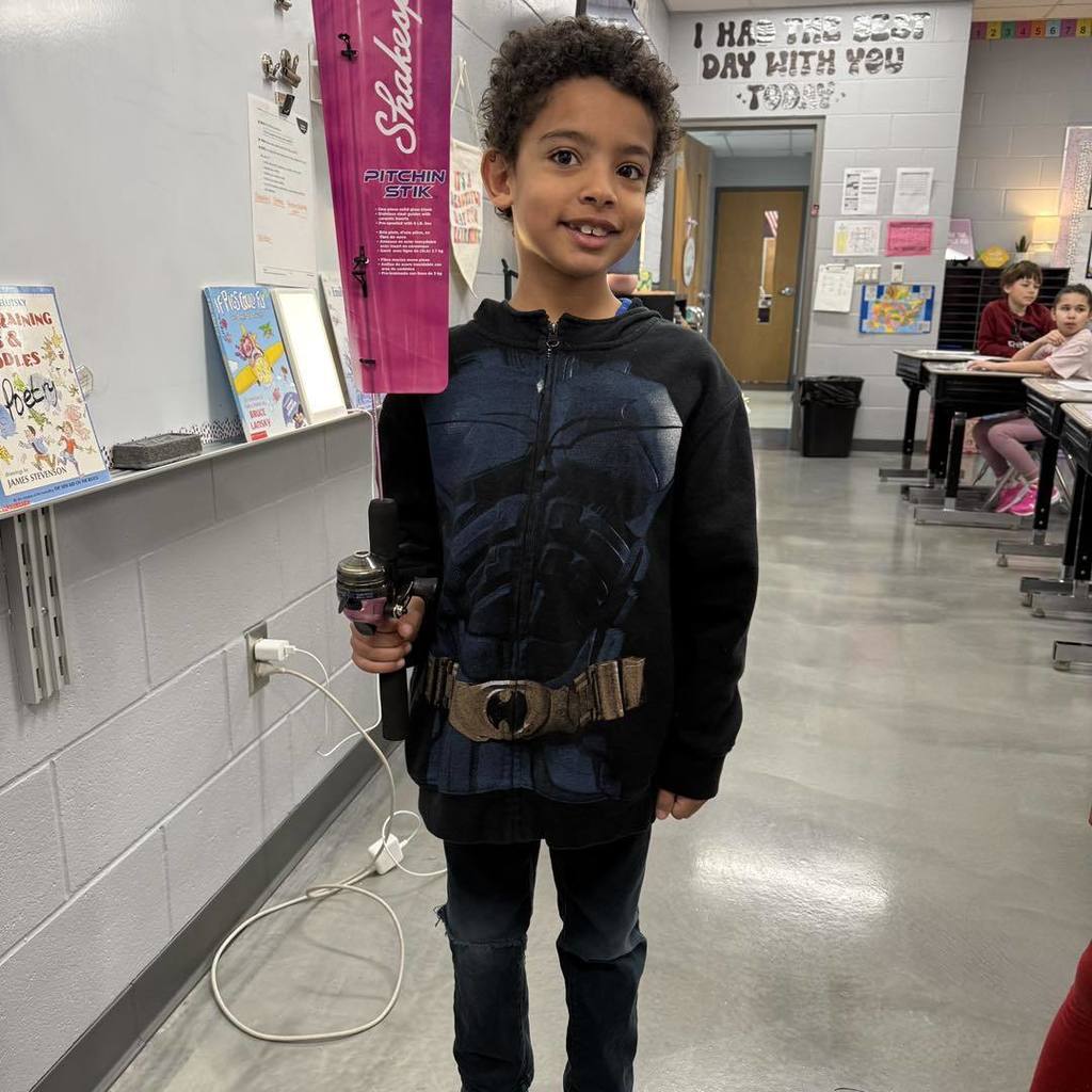 A smiling Unity student standing in a classroom holding a new pink and black fishing rod he earned by saving up behavior tickets