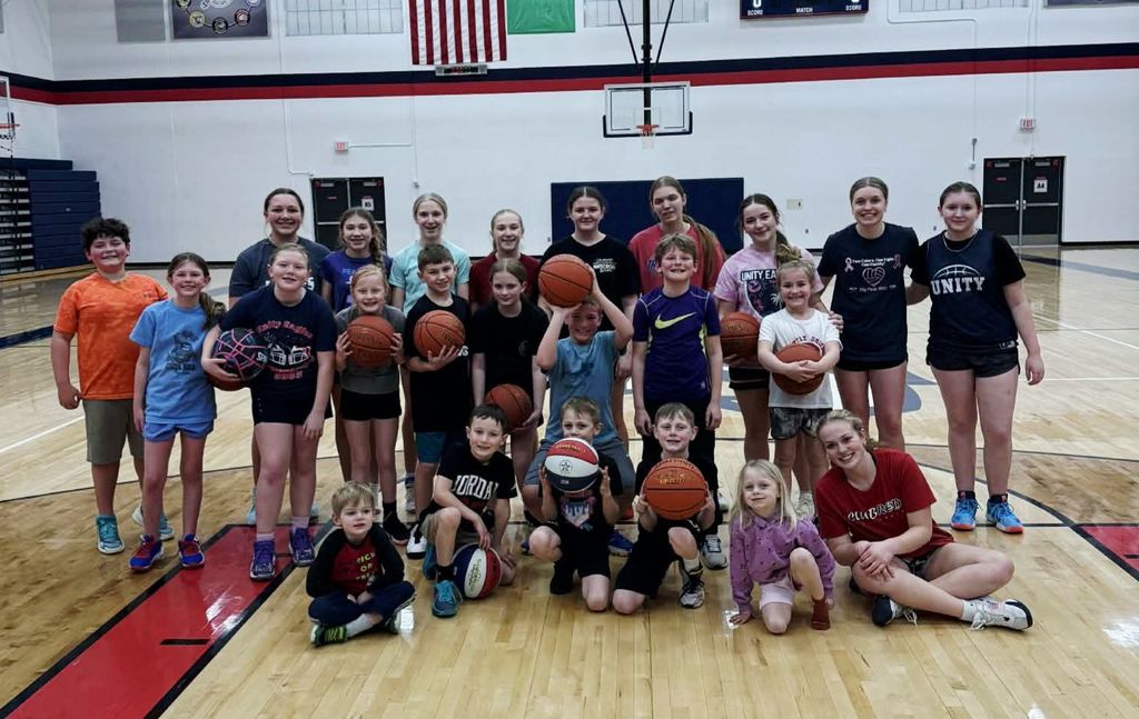 A large group of elementary, middle, and high school students posing with basketballs on an indoor gym court. Some students are wearing Unity School District spirit wear