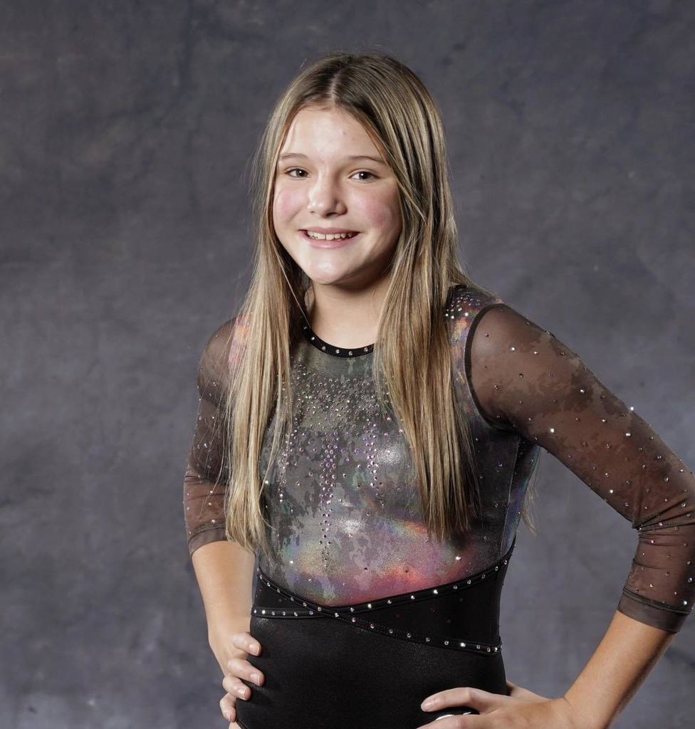 Portrait of Unity student Kinley Filip smiling in a sparkly grey and black gymnastics leotard against a grey studio background.