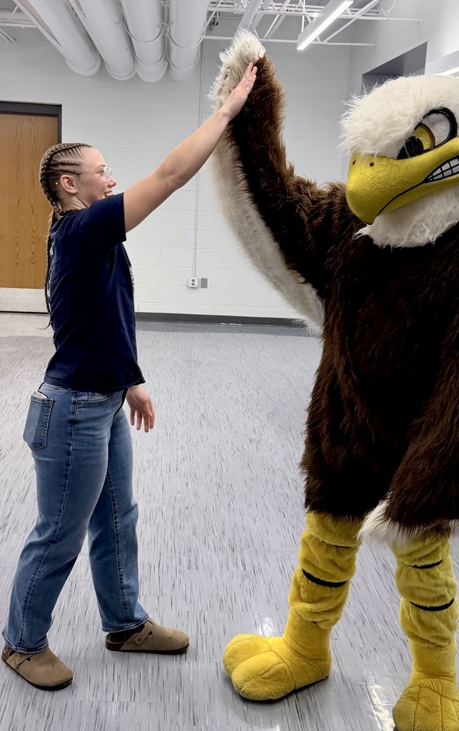 Evelyn Fugate wearing a navy blue shirt and jeans gives a high-five to the Unity eagle mascot in a school hallway.