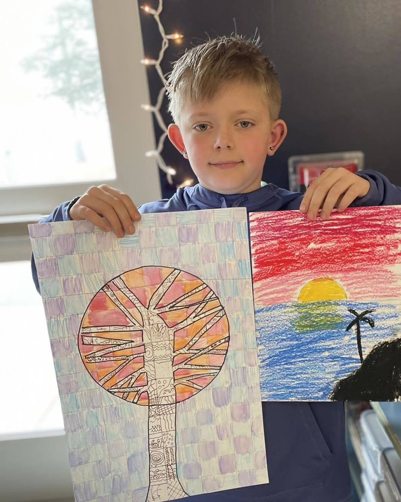 For this new image in your tray, here is the alt text: "A young student at Unity School District proudly holding up two colorful art projects. One drawing features a tree with a large, patterned sun in the background, and the other depicts a sunset over a tropical beach with a palm tree.