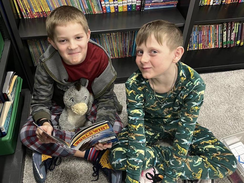 For the first photo in your new set (the two boys in pajamas), here is the alt text: "Two third-grade students sitting together on the floor of a classroom library during Read Across America Week. They are wearing pajamas, and one student is holding a stuffed penguin while they look at a book titled 'Who Would Win?