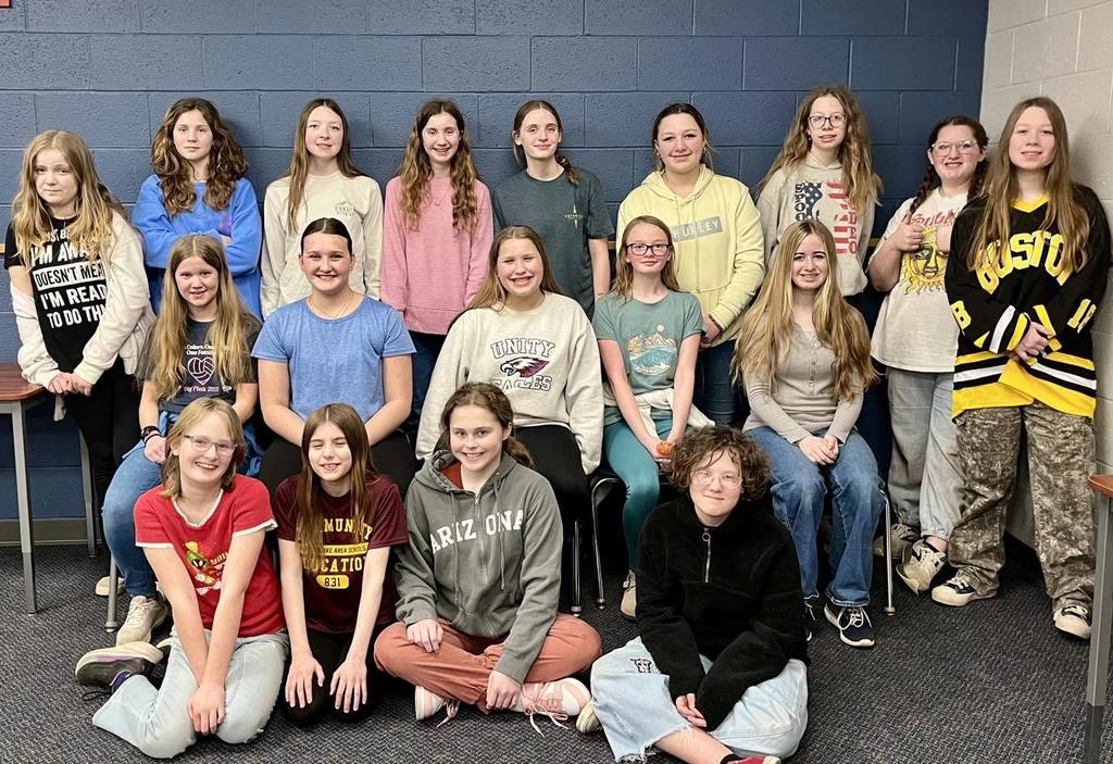 A group of 19 middle school students from the Unity Speech Team posing together in a classroom. The students are arranged in three rows, with some sitting on the floor and others standing, all smiling to celebrate the end of their season."