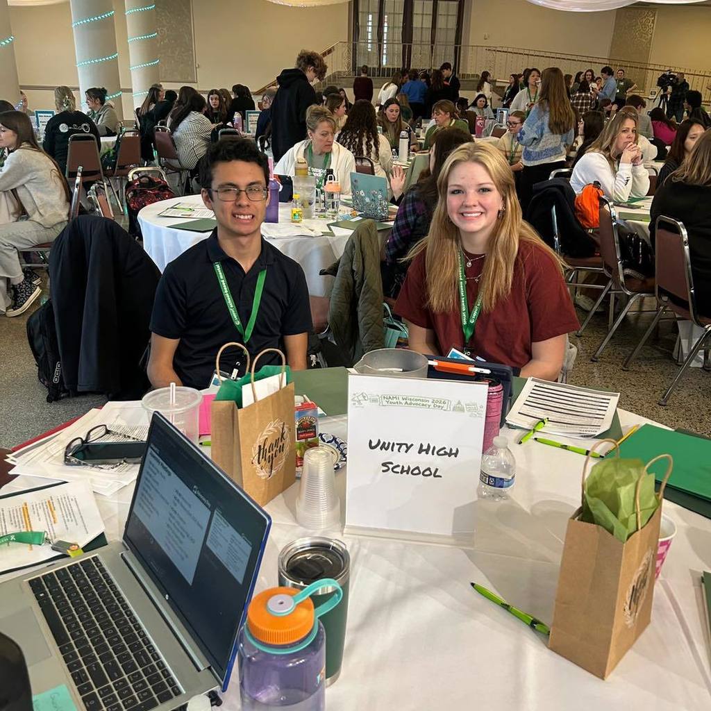 TWO Unity High School students sitting at a table during NAMI Youth Advocacy Day. They are looking at papers and laptops, working together on their advocacy materials in a large conference room.