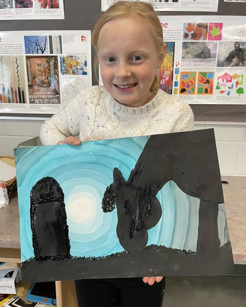 A smiling young girl holding up her painting of a black horse, inspired by her horse Georgie, against a blue and white moonlit background.