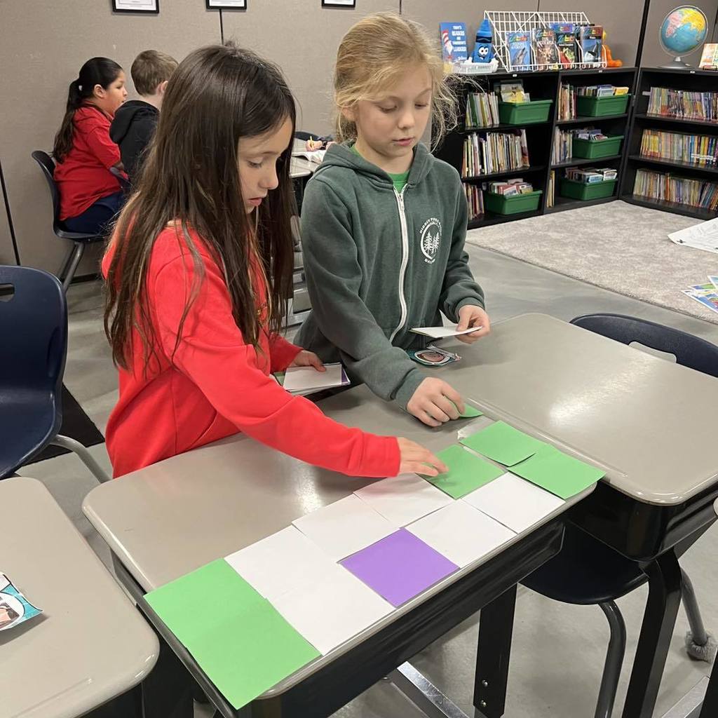 Two young students using colorful square units to tile a desktop during a math lesson on area.