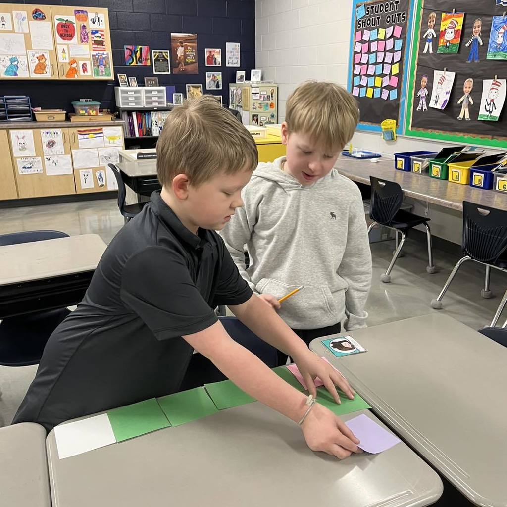Two Unity students collaborating to tile a desktop with colorful square units during a third-grade math lesson on area.