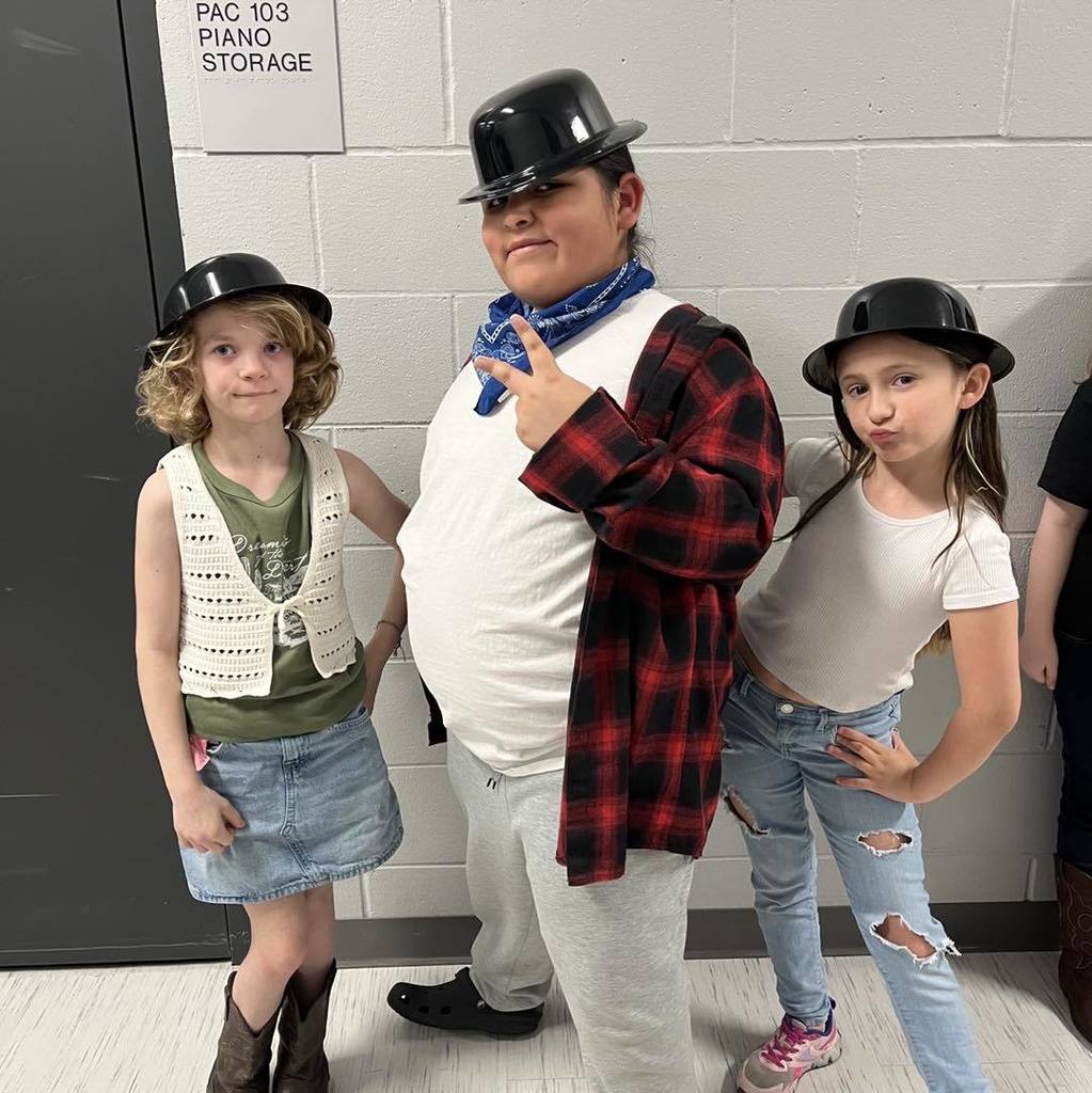 Three Unity third-graders in their concert attire, featuring matching black bowler hats and western-inspired clothing, posing playfully for a photo.