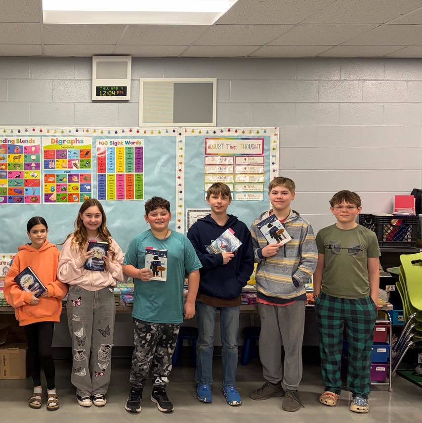 A group of six Unity students posing with their new books in a classroom, showcasing the variety of high-quality reading materials donated by the Marines Toys for Tots Foundation.