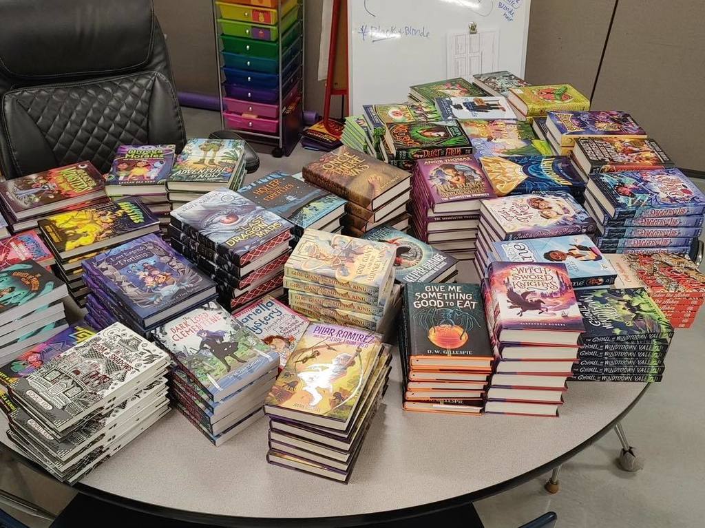 Dozens of colorful new books and graphic novels stacked high on a table, ready to be distributed to Unity students through the Toys for Tots Literacy Program.