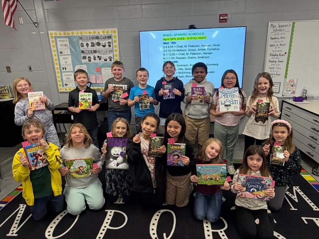 A classroom of Unity elementary students smiling and holding up new books donated by the Marines Toys for Tots Foundation Literacy Program.