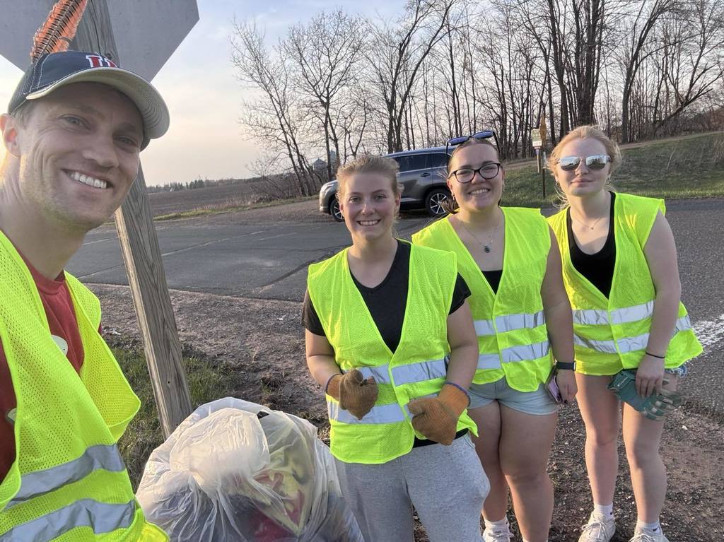 Mr. Mathias and three Unity NHS students wearing safety vests and smiling while posing with a bag of litter collected during their Earth Day highway cleanup project.