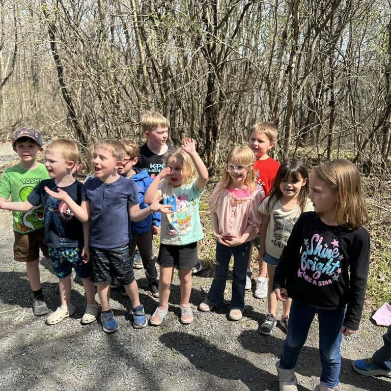 A class of Kindergarten students pausing for a group photo on a sunny wooded path during their Earth Day exploration.