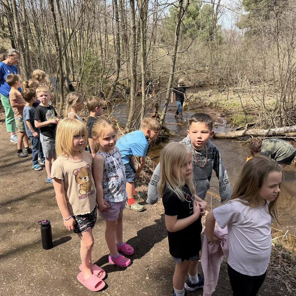A class of Unity Kindergarten students posing in a long line along a scenic forest path next to a stream during their Earth Day nature walk.