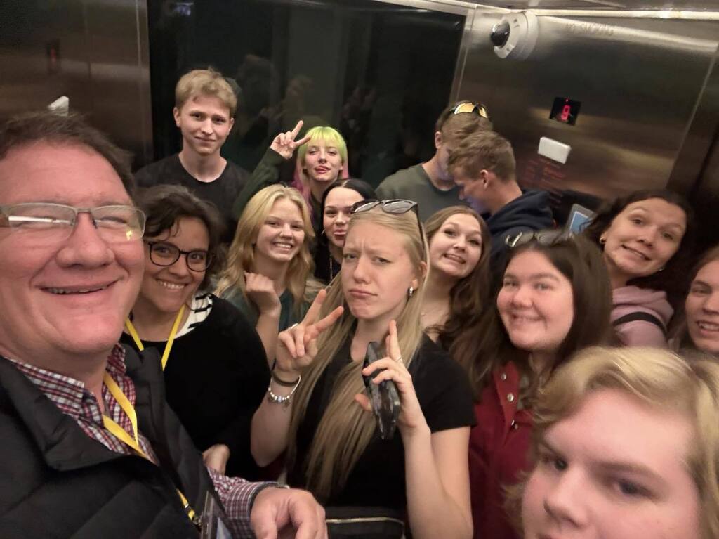 A large group of Unity High School AP Literature students and their teacher smiling and posing for a selfie in an elevator during their field trip to the Guthrie Theater.