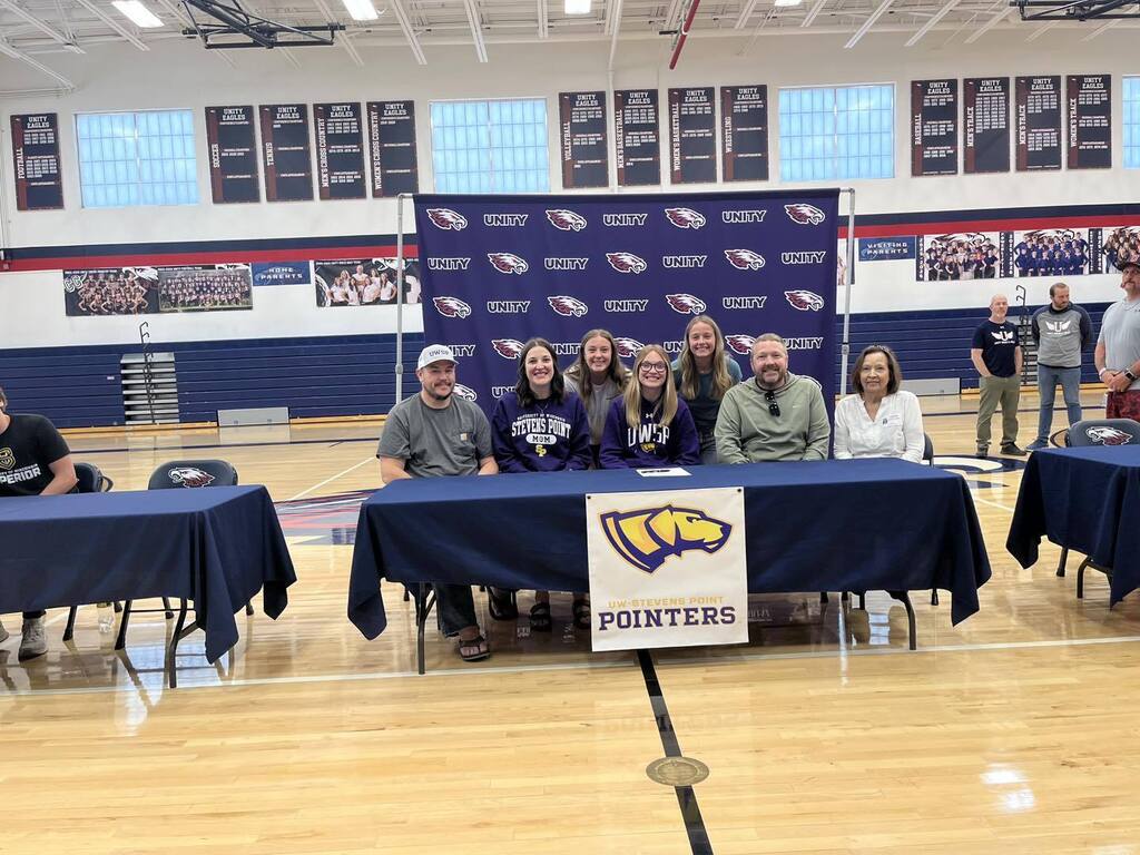 Isabelle Olson sitting at a signing table for the University of Wisconsin-Stevens Point, surrounded by a group of peers and staff