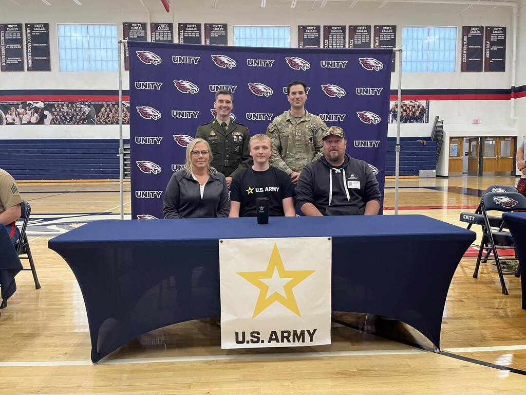 Logan Denver standing at a U.S. Army signing table with a group of family and school staff in the gym.