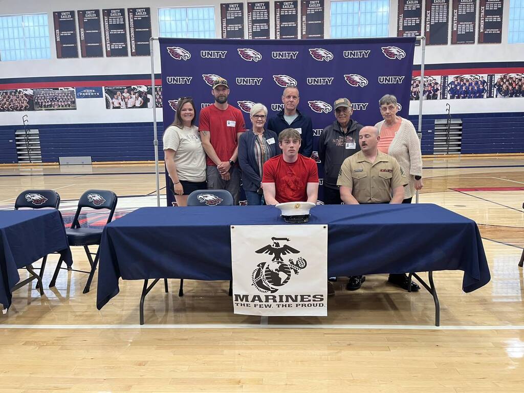 Charlie Livingston standing behind a United States Marine Corps signing table, posing with a group of supporters.
