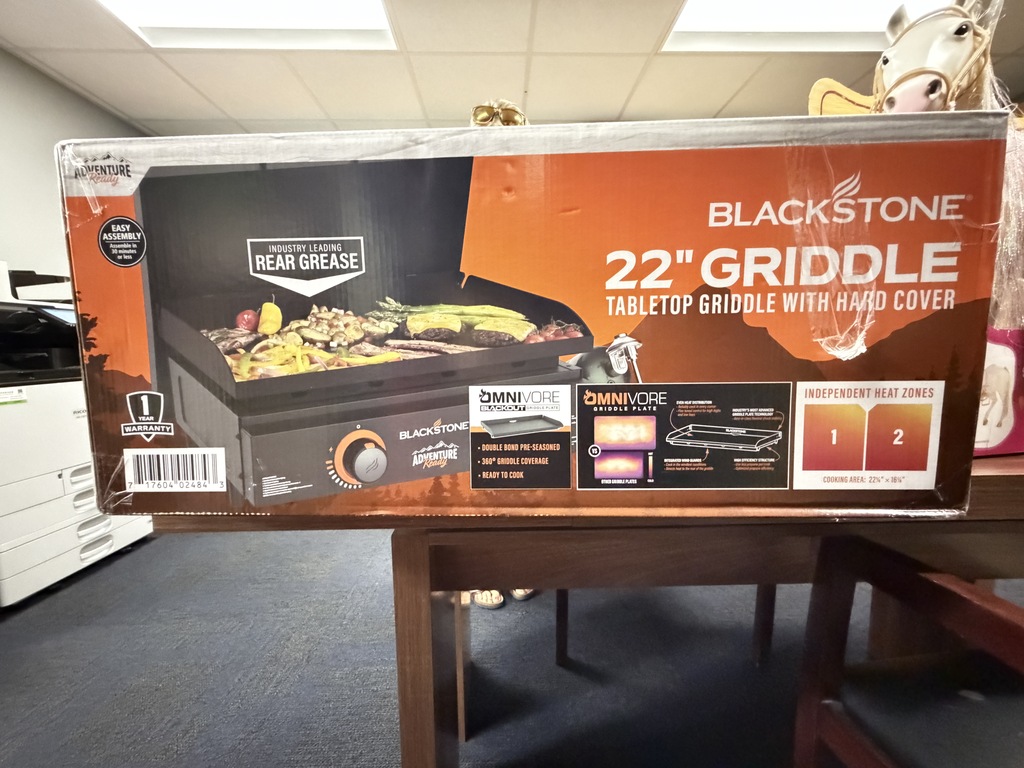 Boxed Blackstone 22" Griddle tabletop griddle with hard cover, shown sitting on a dark wooden table in an indoor room.