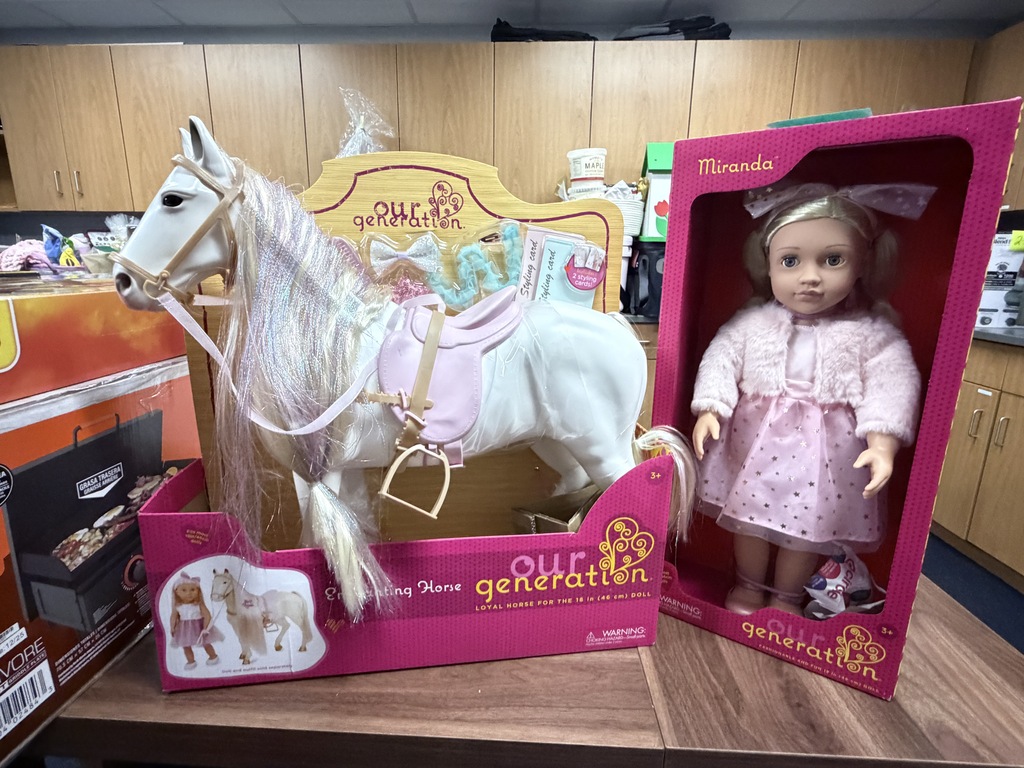 An "Our Generation" doll named Miranda in a pink display box next to a toy horse in an "Our Generation" box.