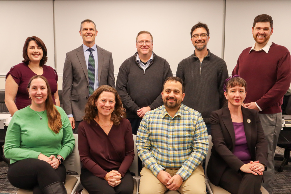 A group of ten people posing indoors, with five seated and five standing.