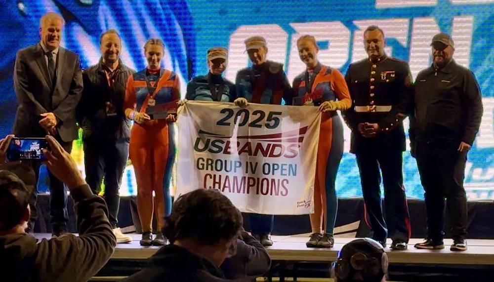 A group of nine people on stage holding a "2025 USBANDS GROUP IV OPEN CHAMPIONS" banner.