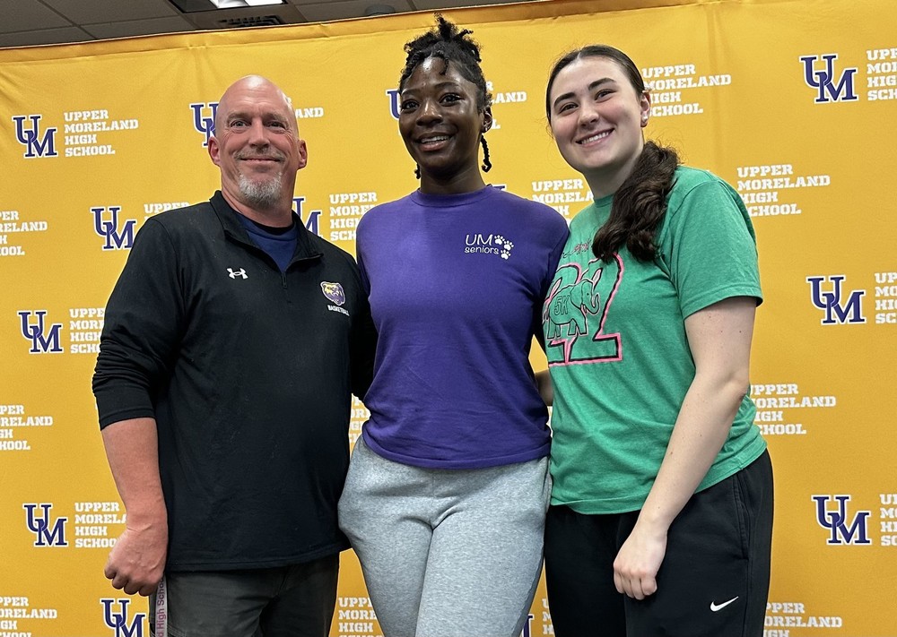 Three individuals smiling in front of a yellow "Upper Moreland High School" backdrop.