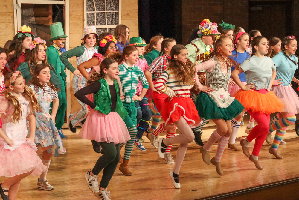 A group of young dancers performing on stage in colorful, whimsical costumes.