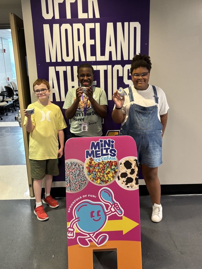 A group of three students hold their Mini Melts Ice Cream and pose for a picture in front of a sign