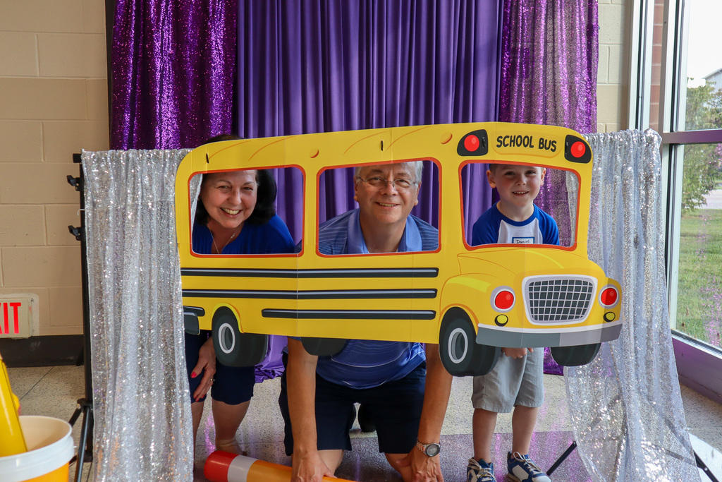 A family posing inside a paper school bus with sparkly silver and purple cloth decorations