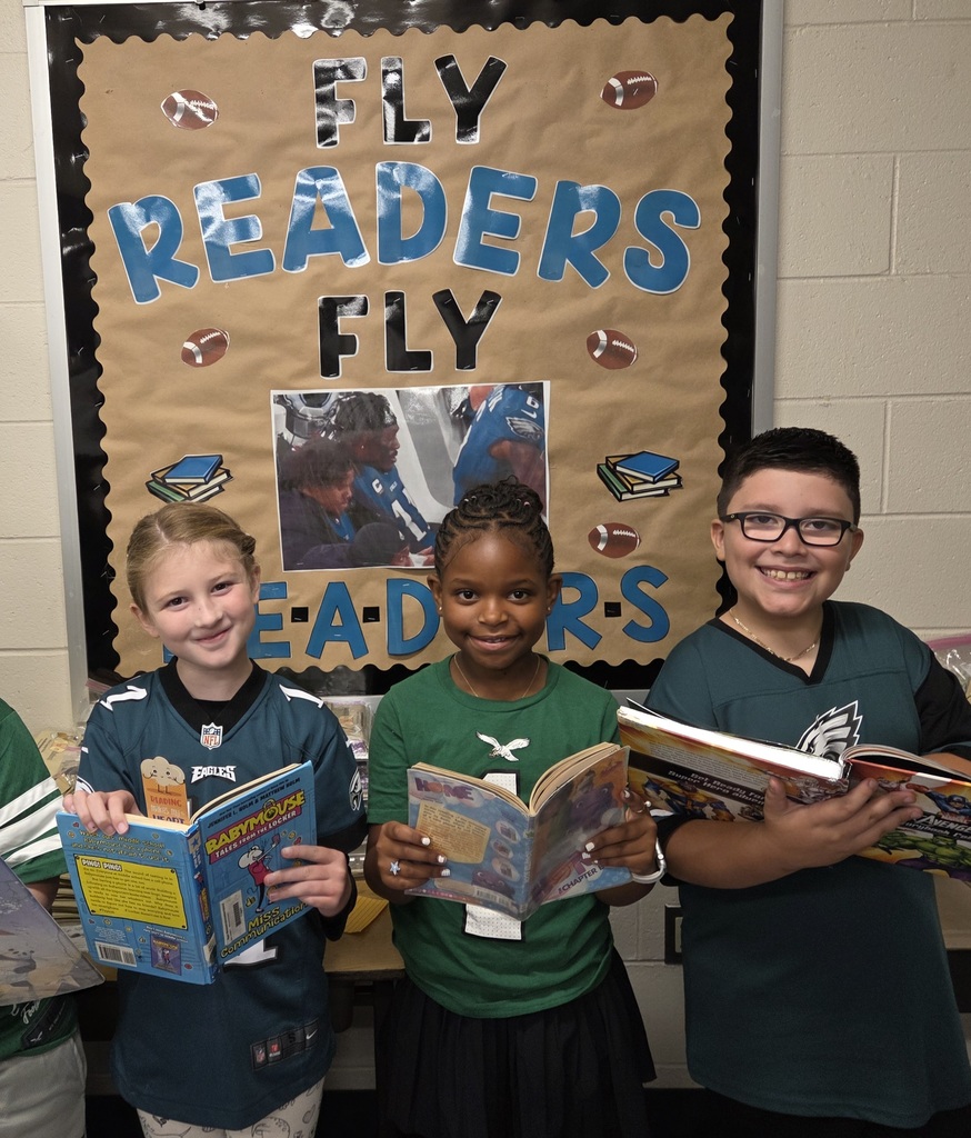 UMIS students pose for a photo wearing their Eagles gear and holding books in front of a sign that says FLY READERS FLY