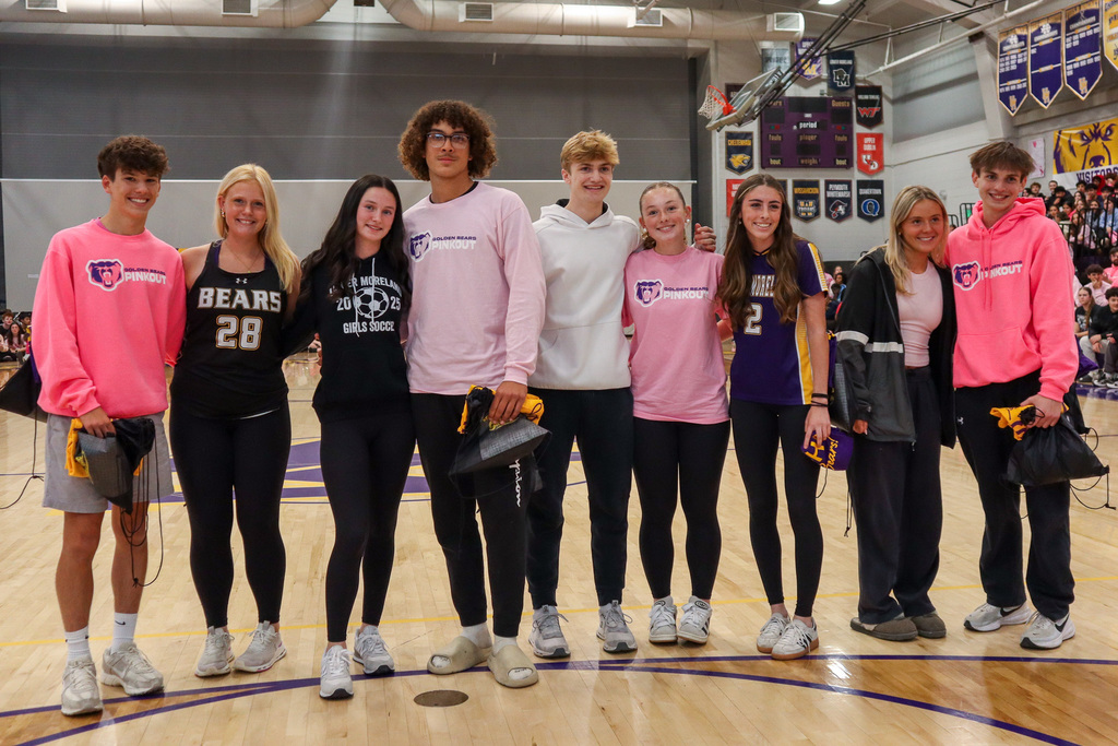 A group of nine people in a gymnasium wearing sports and casual attire, including "Golden Bears Pink Out" shirts.