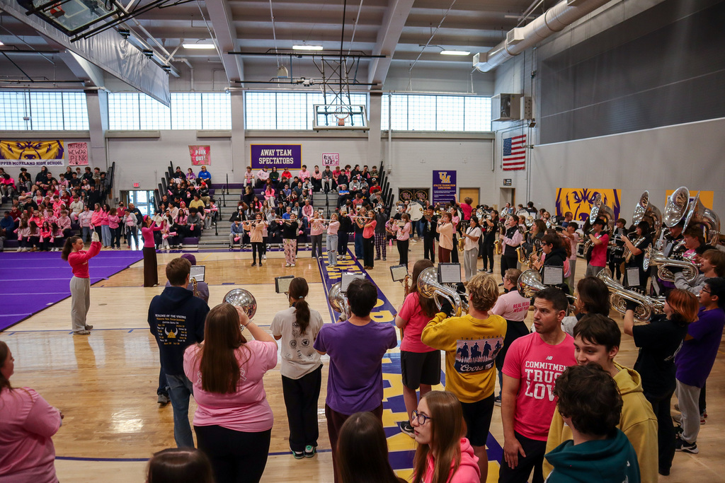 High school marching band playing in a gymnasium with seated spectators and banners on the walls.