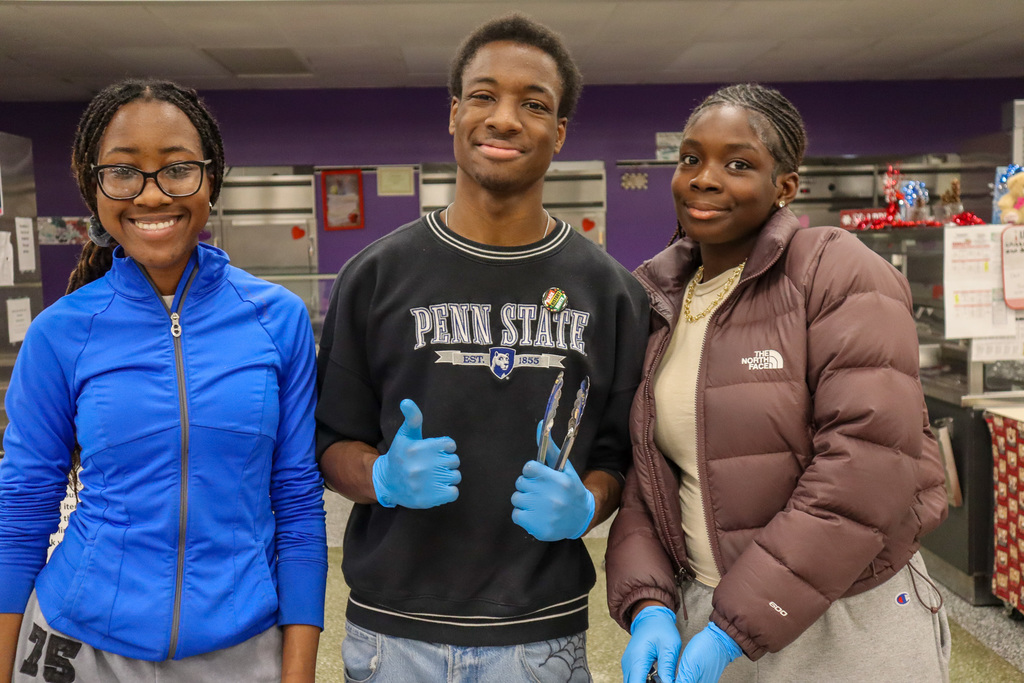 Three people smiling, two in jackets, one in a Penn State sweatshirt, standing indoors.
