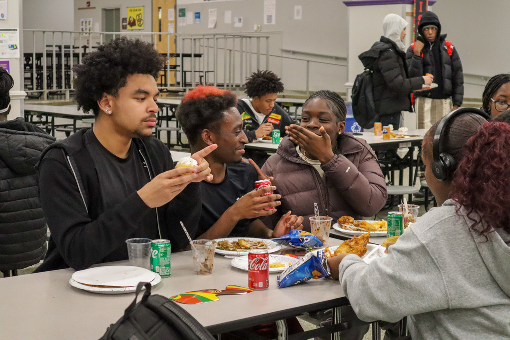 Young people sitting at a cafeteria table, eating and talking.