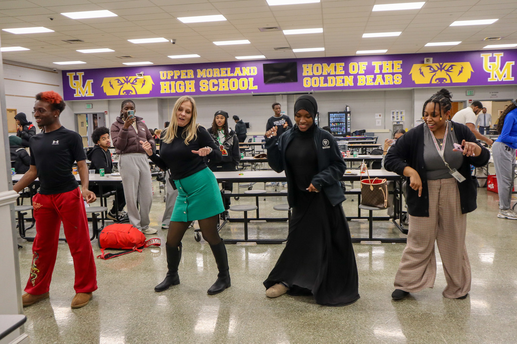People dancing in a school cafeteria with a banner reading "Upper Moreland High School" in the background.