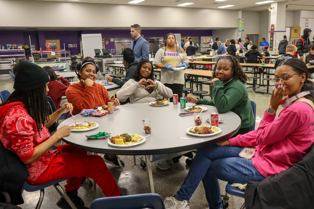 A group of people seated at a round cafeteria table, eating and socializing.