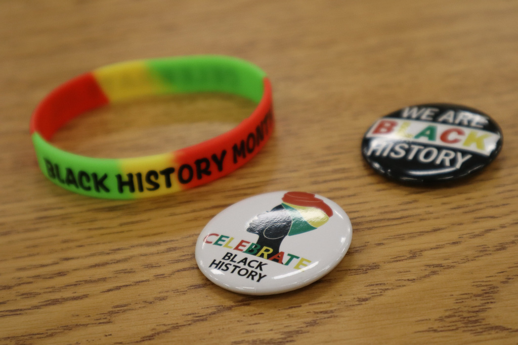 A Black History Month wristband and two thematic badges on a wooden surface.