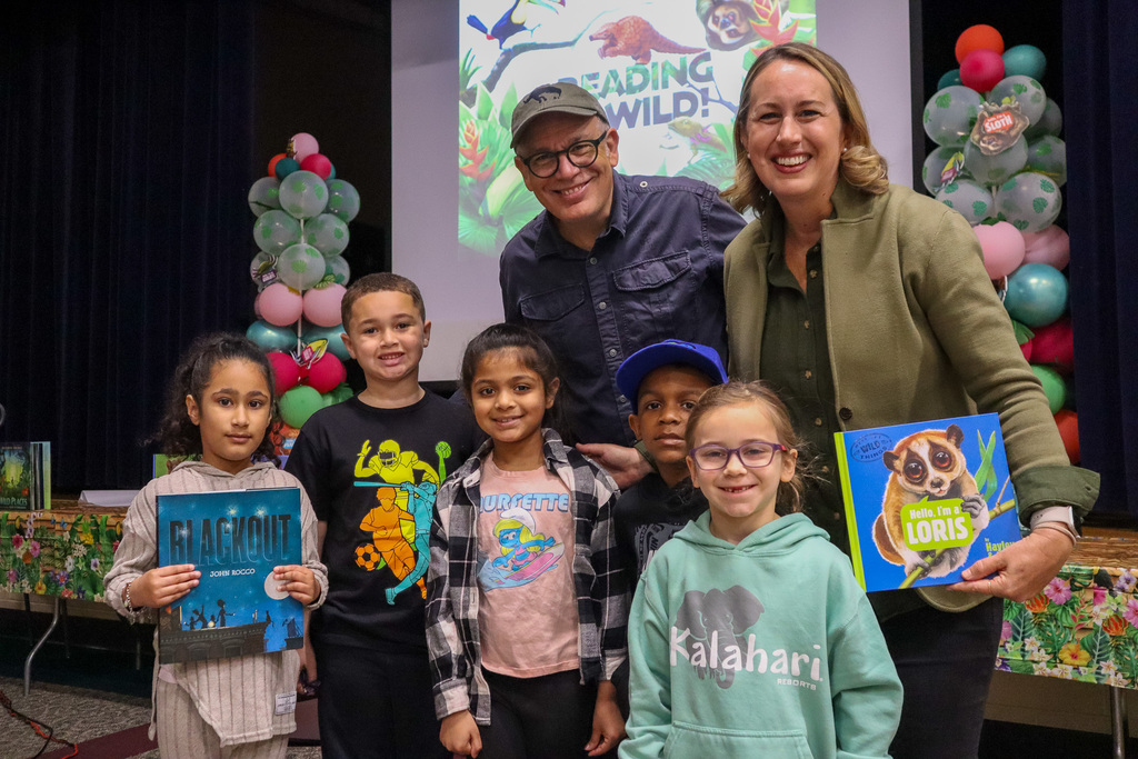 Students hold books and stand alongside authors and illustrators for a group photo